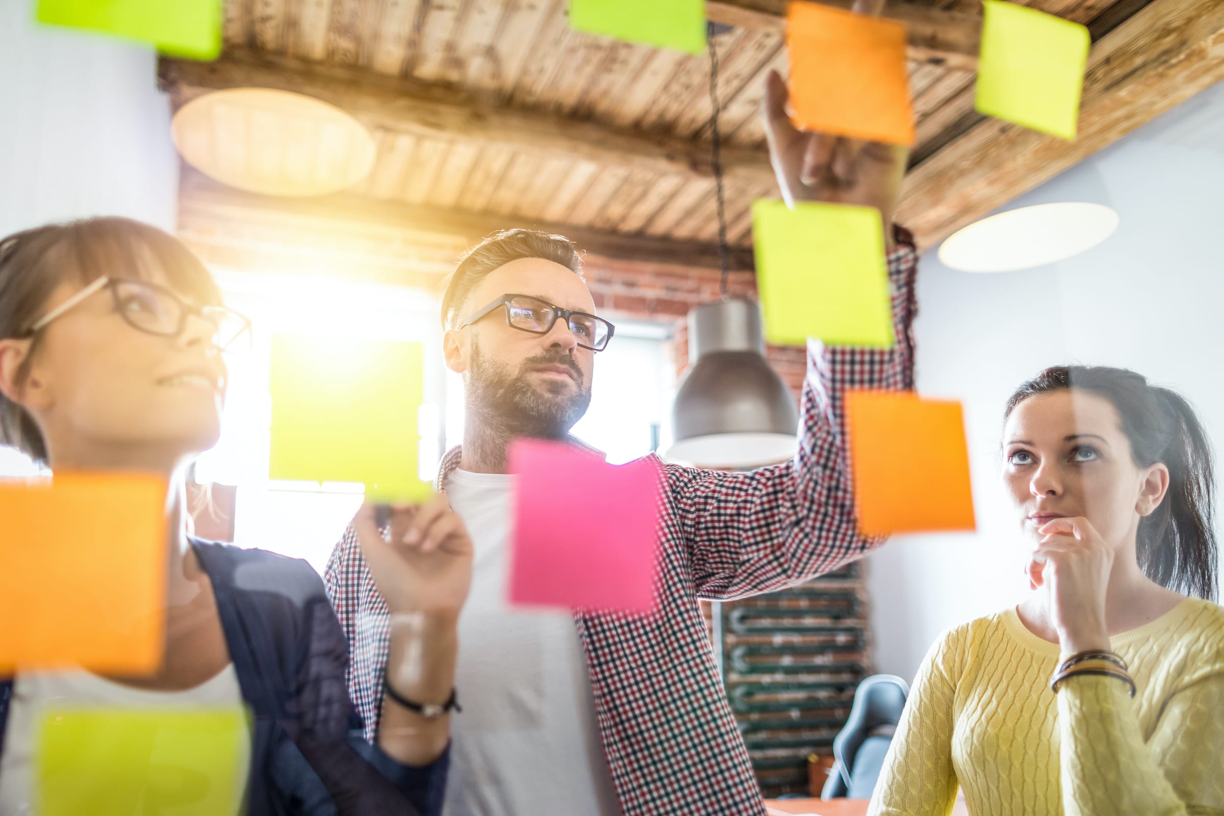 Three of Ventera's product development team organizing sticky notes and solving complex challenges on a glass dry erase board