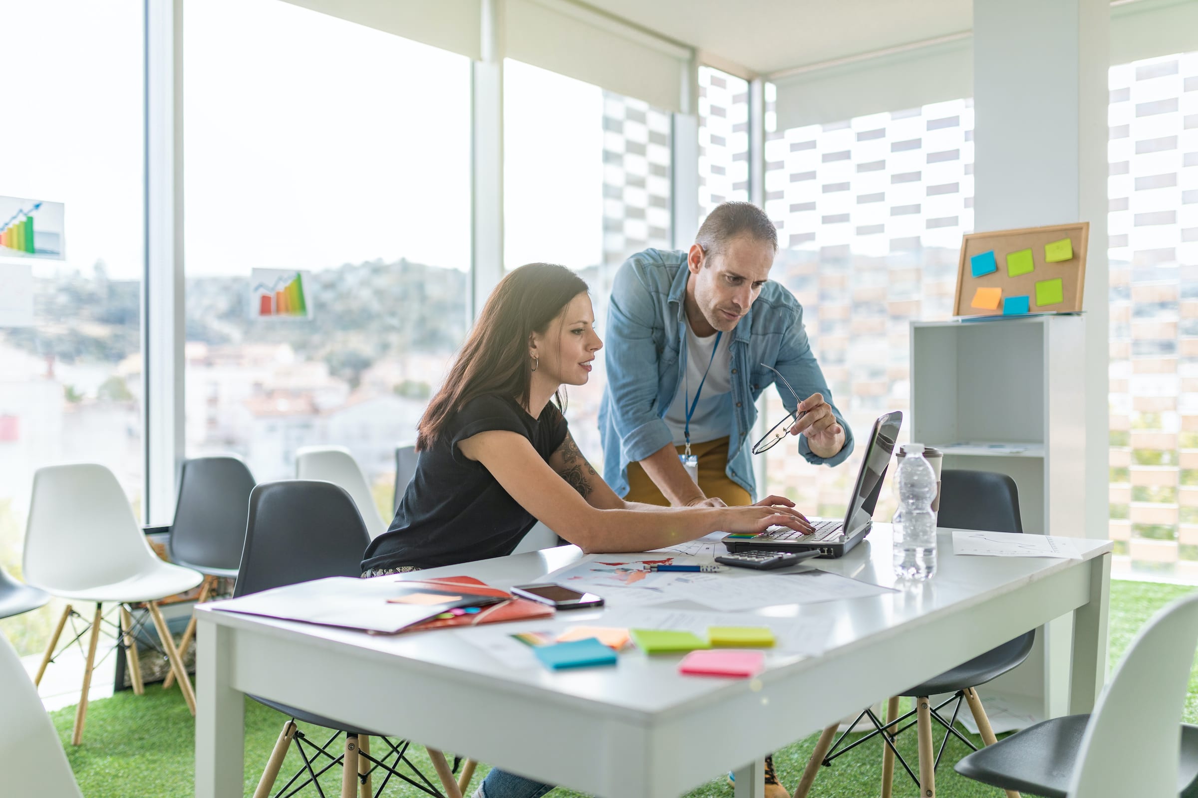 A man and a woman site in a sunny conference room discussing design on a computer