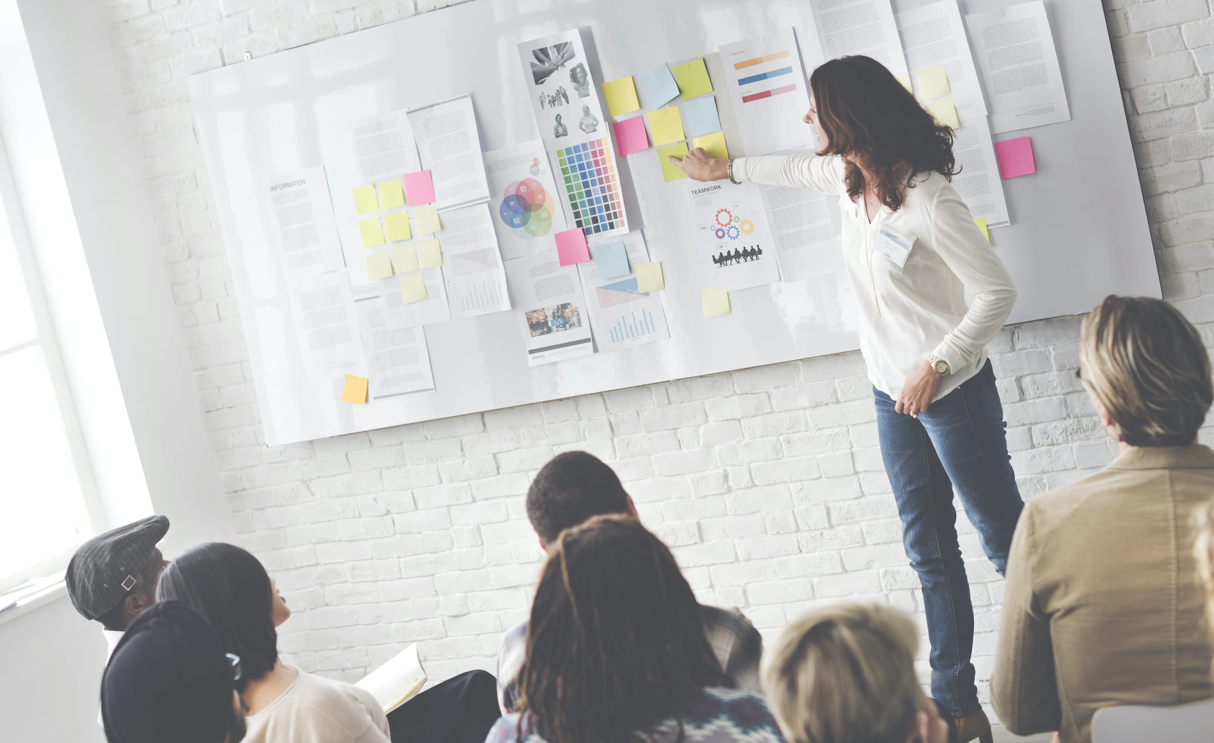 Woman presenting a whiteboard with notes in front of a group of people with notebooks