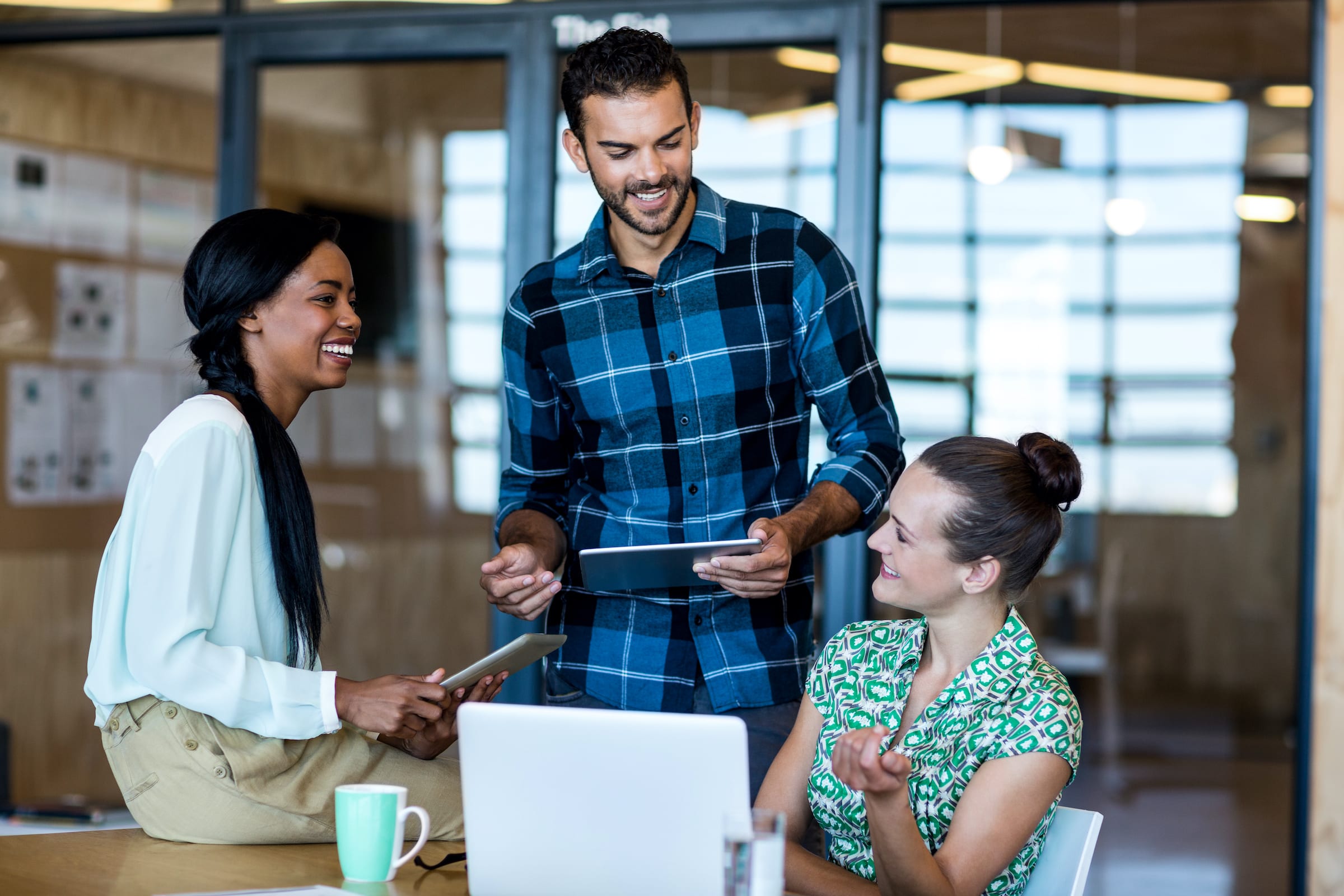 Team of three people smile around table with computer and tablet