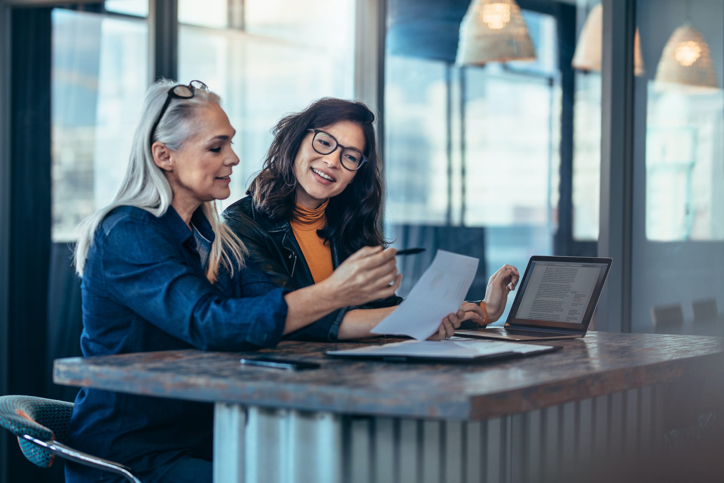 Team of two women sitting at a table with computer collaborating on a project