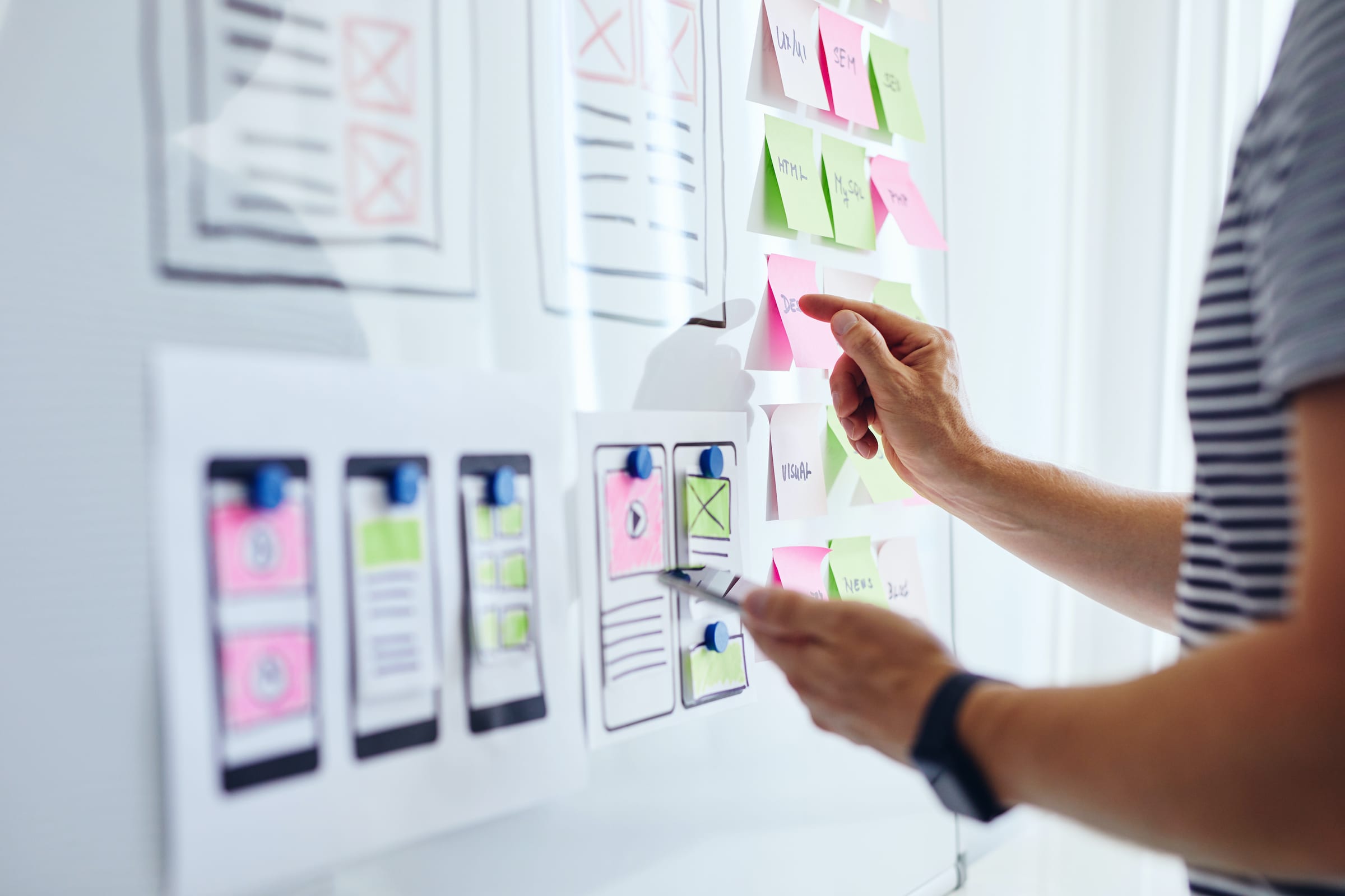 A UX designer reading sticky notes posted on a whiteboard with a moble application wireframe on it