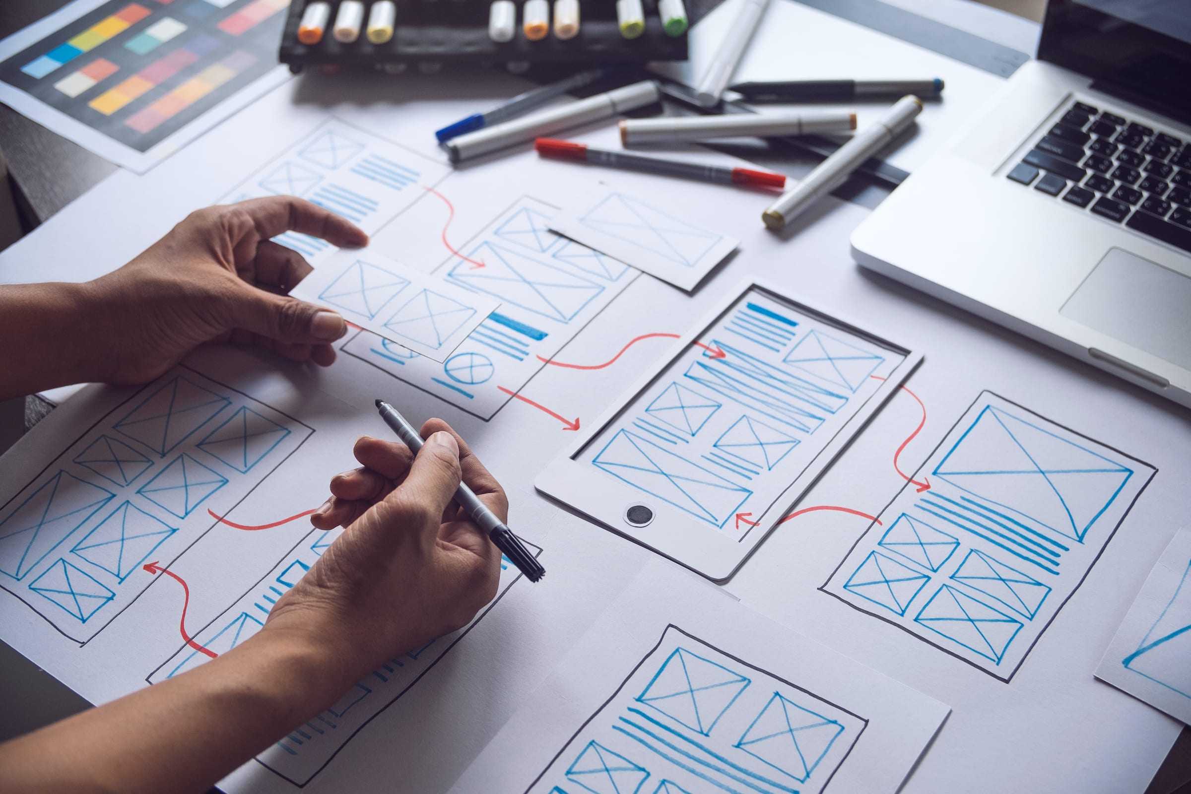 A hand using a marker to edit a mobile application wireframe, with red arrows drawn to indicate the process flow